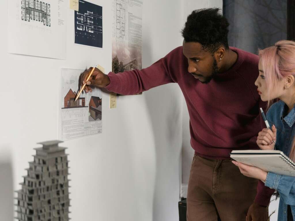 A Man and a Woman Checking the Printed Paper Posted on the Wall