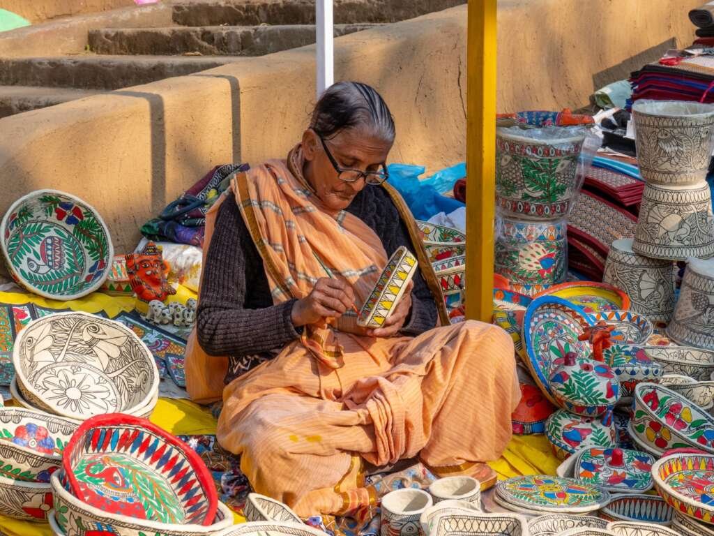 woman sitting on the ground painting trays with her hands using natural pigments