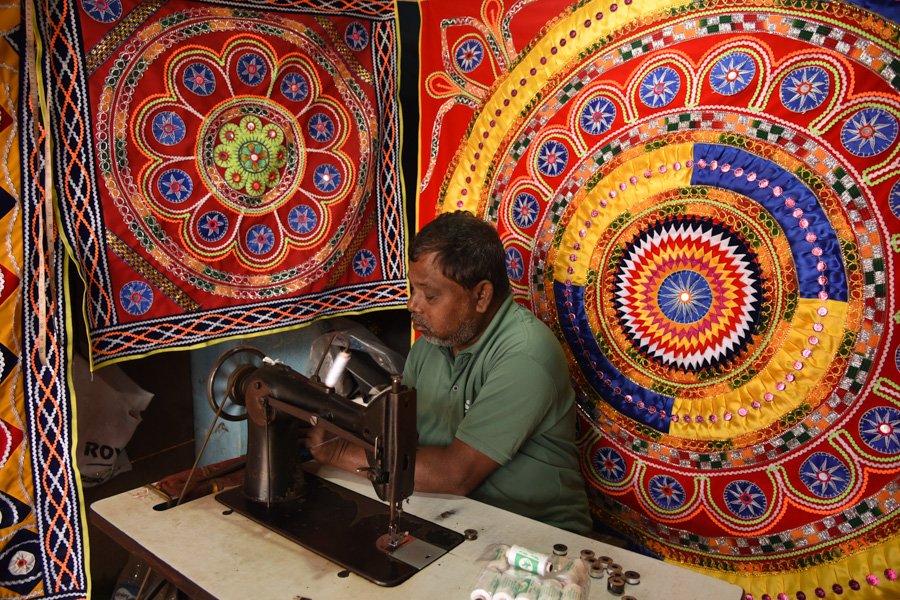 man stitching textiles with a sewing machine surrounded by tapestries