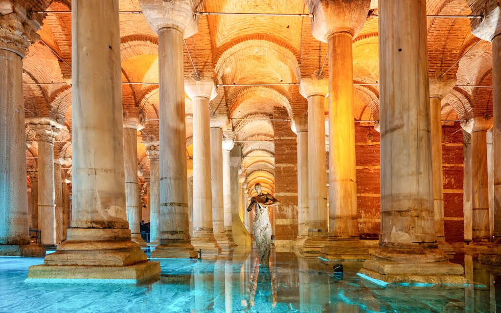 marble sculpture and columns standing amid still water in the basilica cistern, neon lights glowing underwater