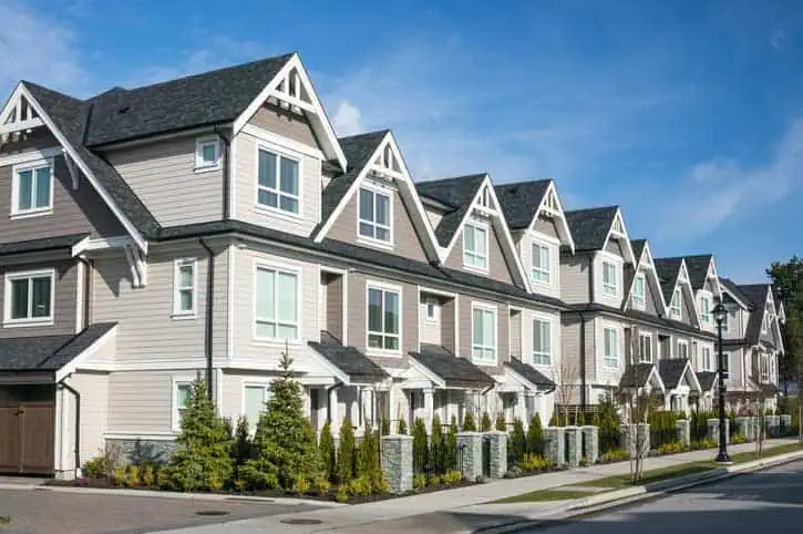 Modern townhouses with gabled roofs, beige and gray siding, and manicured landscaping.