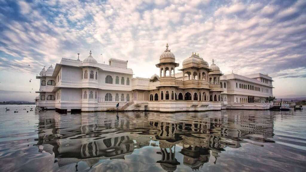 White marble Taj Lake Palace floating on Lake Pichola, showcasing Mughal and Rajput architectural styles with domes, jharokhas, and arches.