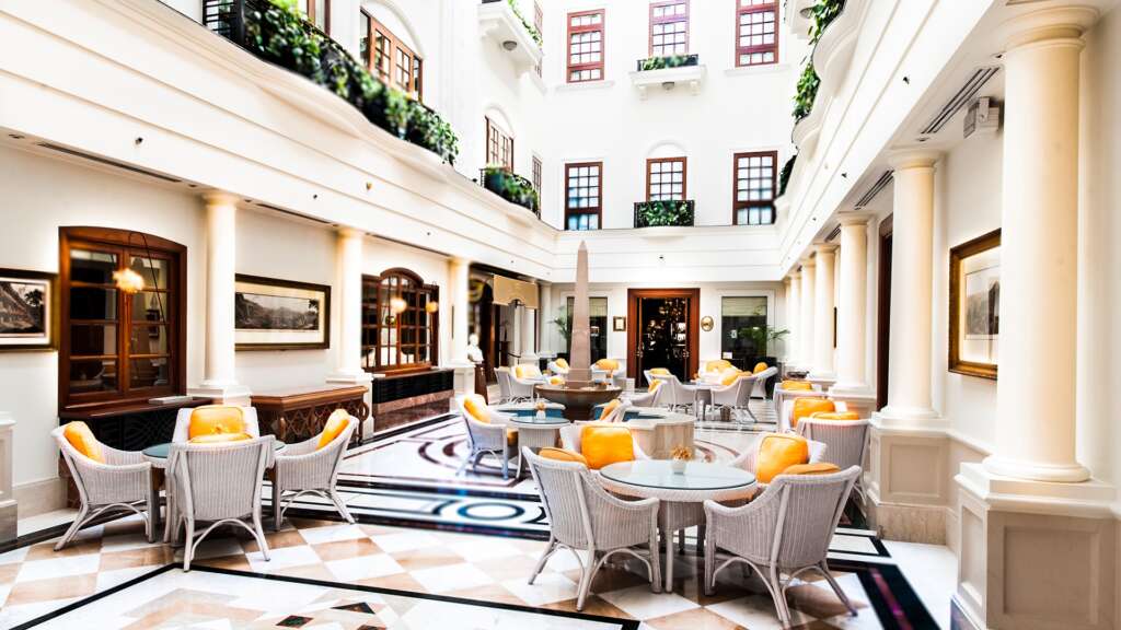 Art Deco and colonial-style white façade of The Imperial Hotel in Delhi with palm-lined drive and classic heritage interiors.

